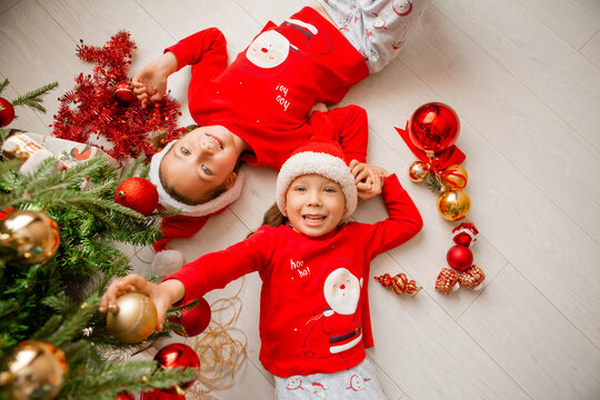 top view of a boy and a girl, brother and sister in red pajamas playing, laughing lying on the floor under a decorated Christmas tree. winter New Year's concept. space for text. High quality photo