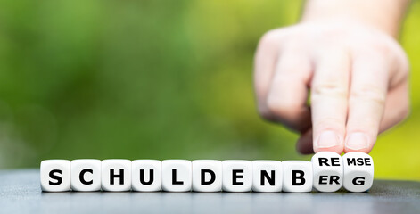 Schuldenberg oder Schuldenbremse. Hand dreht Würfel und ändert das Wort Schuldenberg in...
