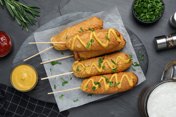 Delicious deep fried corn dogs and sauces on black table, flat lay