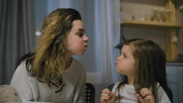 Mom and daughter play games and puff up their cheeks in the evening in the kitchen