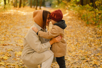 Fototapeta premium Happy young mother and son are walking in the autumn forest. Autumn outdoor activity for family with kids. Happy mother's day. Family day. Autumn day. Happy family leisure.