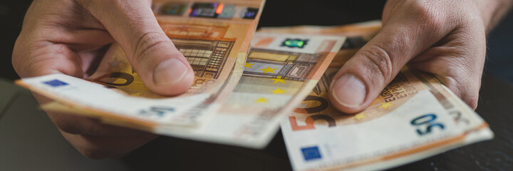 business man counting money. rich male hands holds and count cash banknotes of 50 euros bills or notes currency in front of a laptop. banner