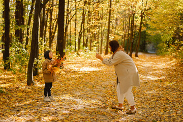 Fototapeta premium Mom and son take a selfie on the phone in the autumn forest. People use technology. Autumn outdoor activity for family with kids. Happy mother's day. Family day. Autumn day. Happy family leisure.