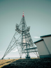 A Radio Tower on a mountain Top. The tower sits on top of the mountain against a blue sky surrounded by rocks and pine trees.