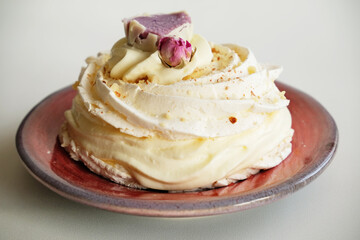 Pavlova dessert decorated with flower on a purple-red ceramic pottery plate on white background