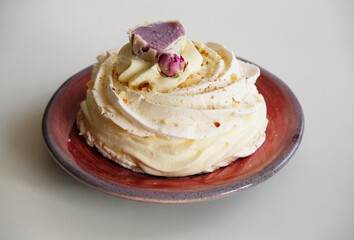 Pavlova dessert decorated with flower on a purple-red ceramic pottery plate on white background
