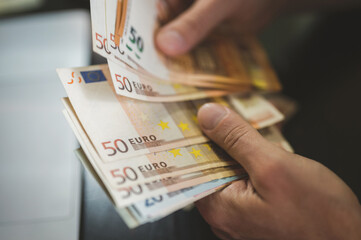 business man counting money. rich male hands holds and count cash banknotes of 50 euros bills or notes currency in front of a laptop