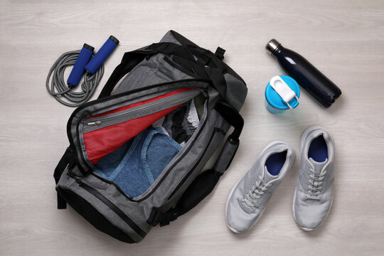Gym bag and sports equipment on wooden background, flat lay