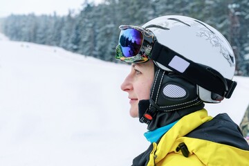 Portrait of a young beautiful woman caucasian ethnicity in a ski helmet and goggles on the background of the ski slope. Bright clothing for active lifestyle and winter sports. Copy space