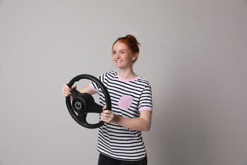 Happy young woman with steering wheel on grey background