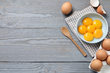 Chicken eggs and bowl with raw yolks on grey wooden table, flat lay. Space for text