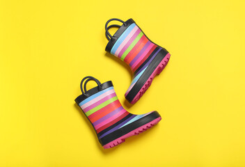 Pair of striped rubber boots on yellow background, top view
