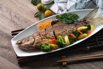 Close up of delicious pan-fried fish dish in a white plate with vegetable.