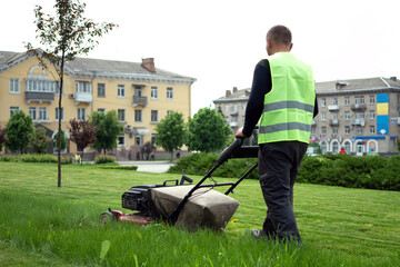 A worker in a vest mows the grass with a lawn mower