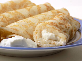 Pancakes stuffed with cottage cheese and sour cream on a plate. Close-up.