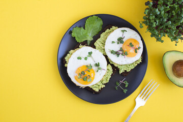 Top view of avocado toasts for breakfast with rye bread, avocado puree, fried eggs and microgreen on the yellow background. Copy space.