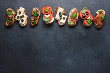 Bruschetta set with prosciutto and basil, tomatoes and mozzarella, camembert and berries, mushrooms and parsley on black background. Antipasto open sandwich appetizer