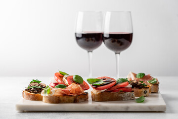 Bruschetta set with prosciutto and basil, tomatoes and mozzarella, camembert and berries, mushrooms and parsley on marble board. Antipasto open sandwich appetizer