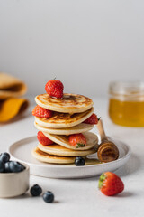 Stack of pancakes with strawberries, blueberries and honey in ceramic plate on white background. Side view, close-up view