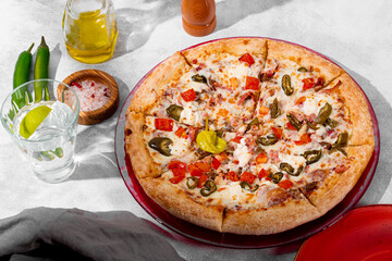 Spicy pizza with chicken, tomatoes and jalapenos on the light gray table