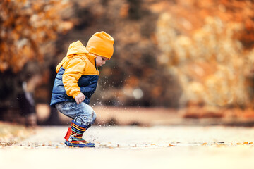 Happy little kid boy jumping on rainy puddle in autumn park