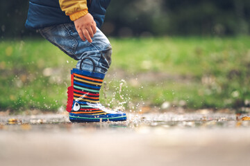 Happy little kid boy jumping on rainy puddle in autumn on nature