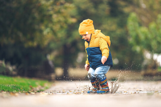 Happy little kid boy jumping on rainy puddle in autumn on nature