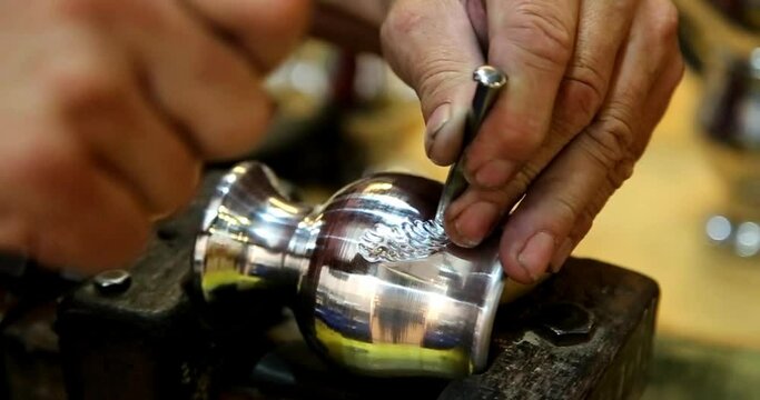 Hands of an Argentine craftsman carving a metal mate. Handwork. Hammer and chisel carving on metal. Close up. Glass to drink the infusion of yerba mate. Argentine tradition.