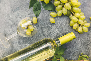 Top view of bottle white wine, green vine, wineglass and ripe grape on vintage gray stone table...