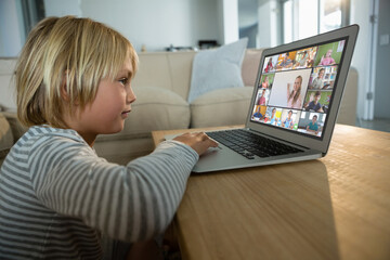 Caucasian boy using laptop for video call, with smiling diverse elementary school pupils on screen