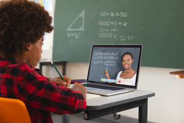 African american boy using laptop for video call, with african american female teacher on screen
