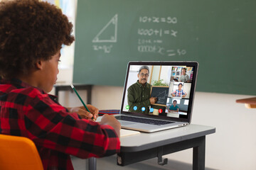African american boy using laptop for video call, with diverse elementary school pupils on screen