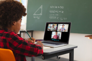 African american boy using laptop for video call, with diverse smiling high school pupils on screen