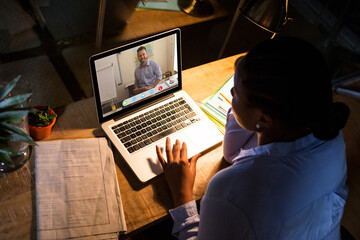 African american woman using laptop for video call, with smiling caucasian male teacher on screen