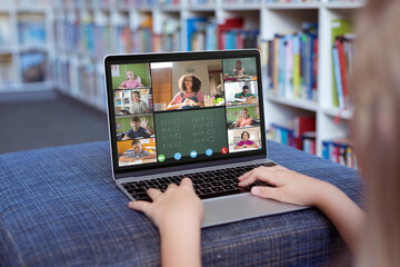 Caucasian girl using laptop for video call, with smiling diverse elementary school pupils on screen - obrazy, fototapety, plakaty