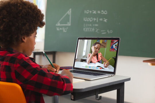 African american boy using laptop for video call, with biracial elementary school pupil on screen