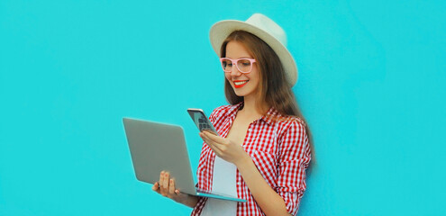 Portrait of modern young woman working with laptop and smartphone on blue background
