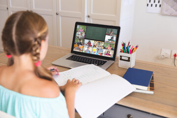 Caucasian girl using laptop for video call, with smiling diverse elementary school pupils on screen