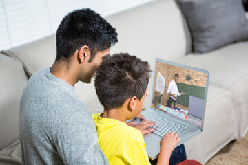 Biracial boy with father using laptop for video call, with male teacher on screen