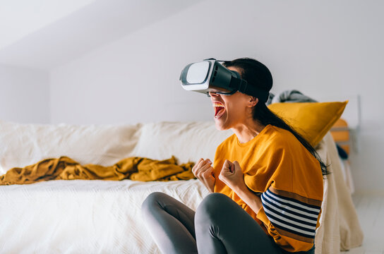Excited casual clothing woman wear virtual reality VR glasses headset in living room. Future trend using virtual reality goggles device for videogame and home entertainment. Futuristic tech experience
