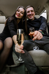 Happy young man and woman drinking champagne in car.