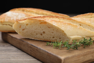 Cut tasty baguette with thyme on wooden table, closeup