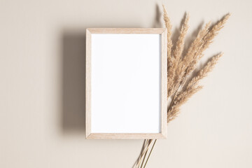 Empty wooden mockup photo frame and dried grass decoration on beige background. Flat lay, top view, copy space