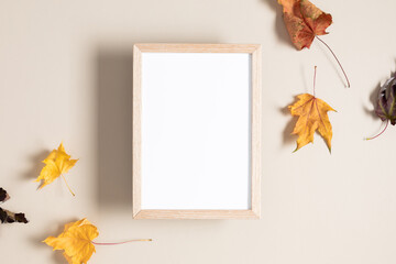Empty wooden mockup photo frame and autumn leaves on beige background. Flat lay, top view, copy space