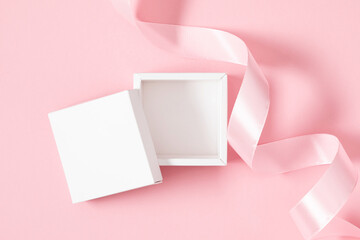 Open gift box mockup with satin ribbon on pastel pink background. Flat lay, top view, copy space
