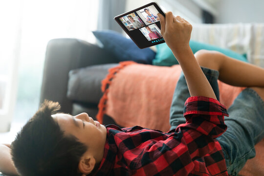 Smiling asian boy using tablet for video call, with diverse elementary school pupils on screen