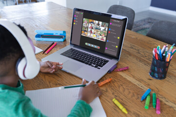 African american boy using laptop for video call, with elementary school pupils on screen