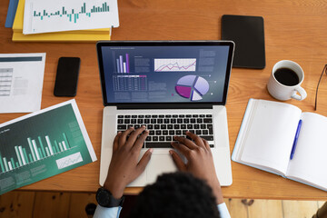 African american businessman sitting at desk using laptop with graph and statistical data on screen
