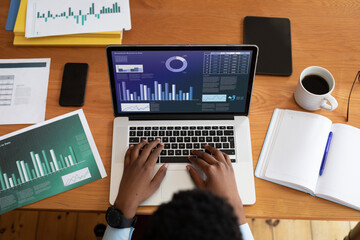 African american businessman sitting at desk using laptop with graph and statistical data on screen