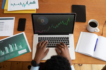 African american businessman sitting at desk using laptop with statistical data on screen
